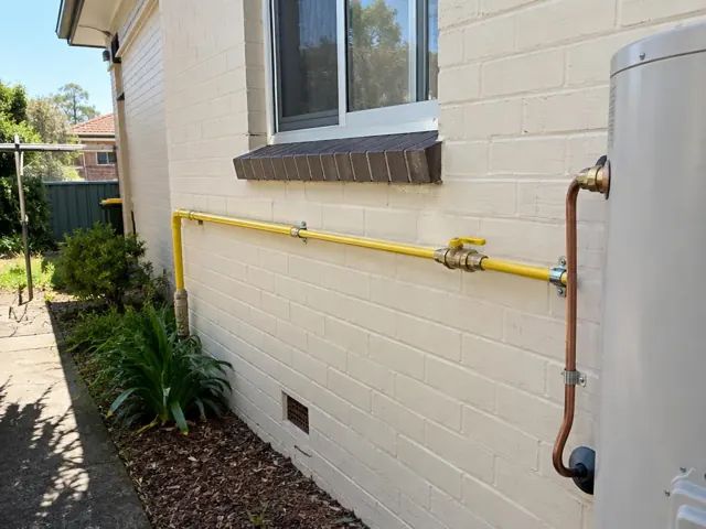 Yellow gas pipe on a painted brick exterior wall beside a hot water unit in Malabar