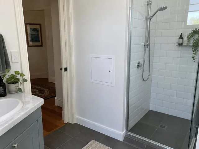 Bathroom wall with a small access panel beside a tiled shower and vanity in Coogee